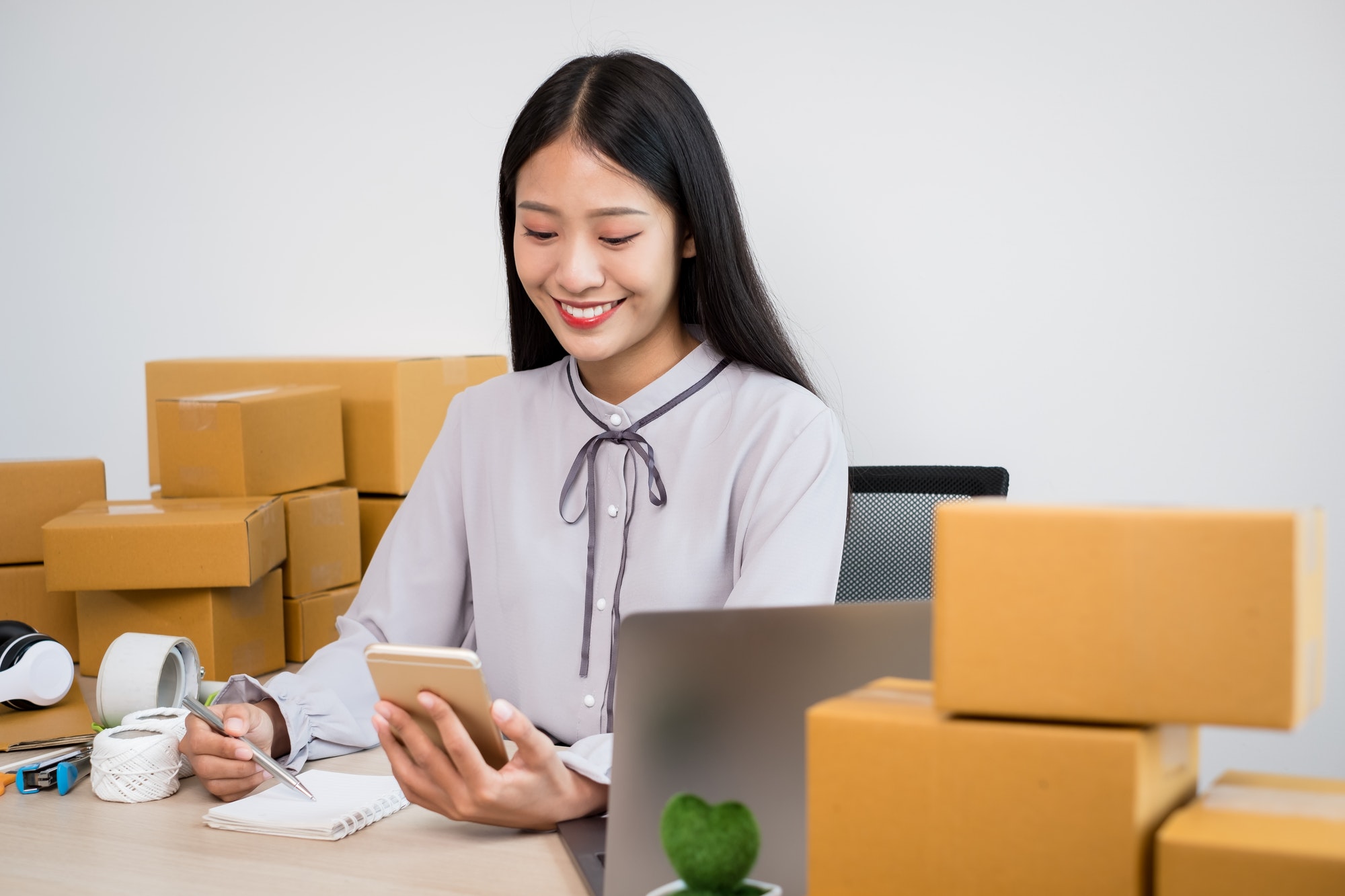 Young Asian woman business owner with many parcel boxes on the table happy online sales job, use you